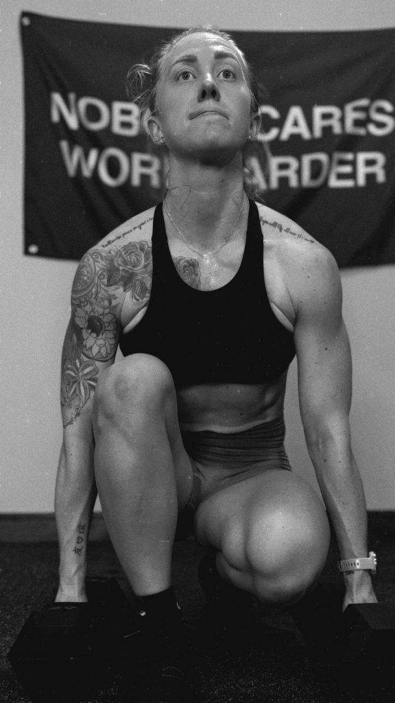 Athlete with tattoos performing a dumbbell exercise in a gym, with a motivational banner reading 'Nobody Cares, Work Harder' in the background.